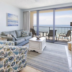 The living area features a comfortable sofa, vibrant shell-patterned chairs, and a TV, all with a stunning beachfront view