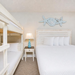 This cheerful guest bedroom features a cozy twin bunk bed and a queen bed, accented by beach-themed decor and soft lighting