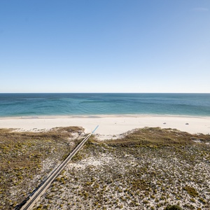Expansive view of the tranquil gulf and white sand beach, framed by coastal vegetation and a wooden boardwalk