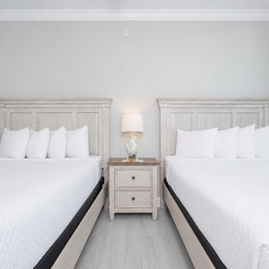 Rest in this cozy guest bedroom featuring two queen beds, soft linens, and a bedside table with a decorative lamp