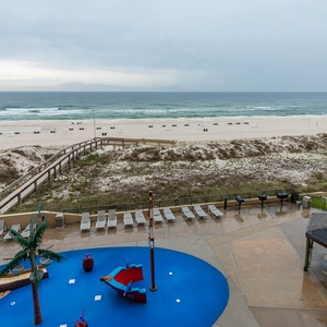 The vibrant pool area features a playful pirate ship splash park and overlooks the beach with lounge chairs along the shore
