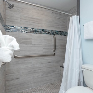 Master bath featuring a walk-in shower with a glass tile accent and a modern toilet beside neatly arranged towels