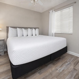 The bedroom features a king bed with crisp white linens, a stylish nightstand, and natural light from the window