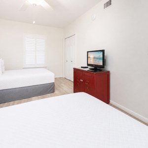 Relax in this comfortable guest bedroom featuring two double beds, a TV for entertainment, and natural lighting