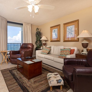 The living area features a light sofa with queen sleeper, leather chairs, and expansive views of the beach