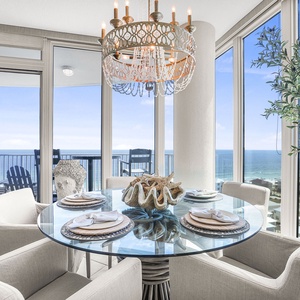 This dining area features a chic glass table with elegant decor and offers a stunning beach view through large windows