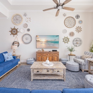 Spacious living area featuring blue sofas with a queen sleeper, coastal decor, and a large TV with a serene beachfront view