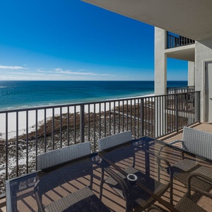 Balcony with a glass table and chairs offers a serene view of the tranquil gulf and white sand beach below