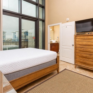 This bedroom features a comfortable queen bed, a TV for entertainment, and large windows offering a bright view