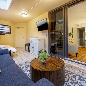 Cozy patio area features a twin/full bunk bed, flat-screen TV, and rustic coffee table, with access to a bright outdoor space