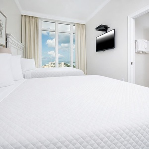 Rest comfortably in this guest room with two queen beds, a mounted TV, and large windows offering beautiful beach views