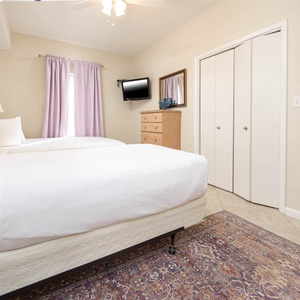 Bright guest bedroom featuring two twin beds, a mounted TV, and soft purple curtains, creating a serene and restful ambiance