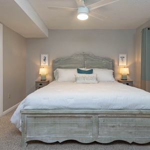 The master bedroom features a stylish king bed with a light wood frame, soft bedding, and calming blue accents