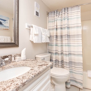This bathroom features a stylish granite countertop, a large mirror, and a striped shower curtain for a fresh feel