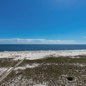 Expansive view of the beach with white sand and umbrellas, framed by a clear blue sky and gentle waves of the gulf