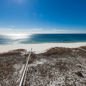 Expansive view of the tranquil gulf waters and white sand beach, framed by natural coastal vegetation and wooden walkways