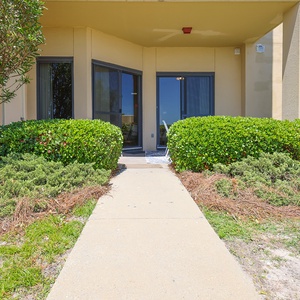 Welcoming patio entryway features lush greenery and a pathway leading to a bright, inviting space with large windows