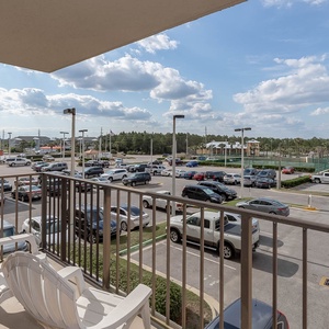 The master balcony view showcases a bustling parking lot with a mix of cars and a glimpse of nearby recreational facilities