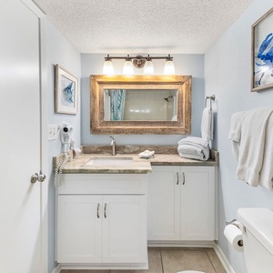 The guest bath features a stylish vanity with a large mirror, decorative art, and plush towels, creating a serene atmosphere
