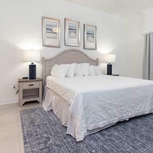 Drift to sleep on the king bed beneath coastal prints with warm lamp light in this guest suite