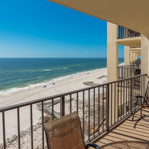 The balcony offers a serene view of the tranquil beach and gentle waves, with comfortable seating for relaxation