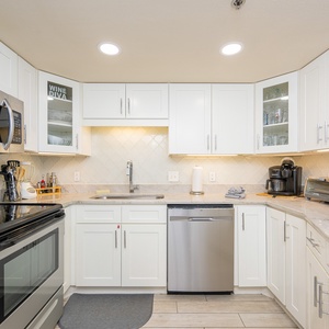 Modern kitchen features sleek white cabinetry, stainless appliances, and a stylish marbled countertop with a breakfast bar