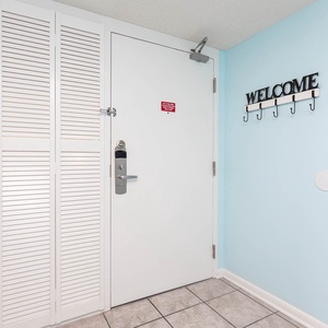 A welcoming entryway features a light blue wall, a white door with a secure lock, and a decorative hook rack for convenience