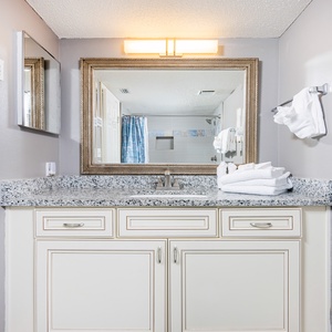 Granite countertop, fresh towels, and a shower area featuring a blue curtain and tile accents comlement this guest bath