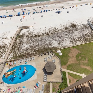 Balcony view overlooking the pool area and pirate ship splash park, surrounded by lounge chairs and boardwalk to the beach
