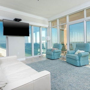 Unwind in the spacious living area, featuring a large TV, comfortable seating, and panoramic beach views