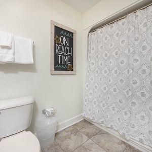 This bathroom features a charming beach-themed sign, soft white towels, and patterned shower curtain for a refreshing retreat