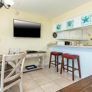 The dining area features a round table, stylish chairs, and a well-equipped kitchen with bar seating for a relaxed meal