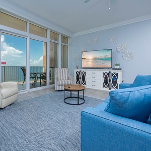 Relax in the airy living room, featuring plush seating and a large TV, with stunning views just beyond the glass doors