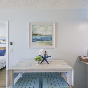 This inviting space features a charming dining table with coastal decor, leading to a cozy bedroom view beyond