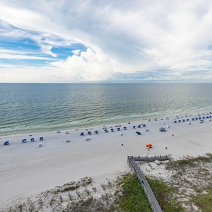Beachfront scene features blue umbrellas lining the white sand, inviting relaxation under a bright sky