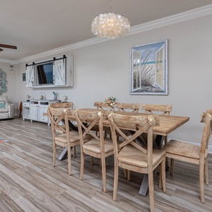 Brightly decorated living area features a wooden dining table, comfortable seating, and a stunning beachfront view