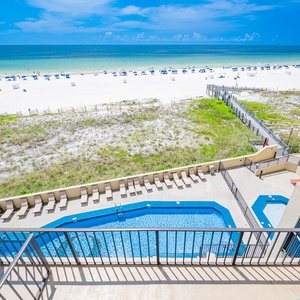 Beachfront view with a sparkling pool and lounge chairs, framed by lush greenery and white sand