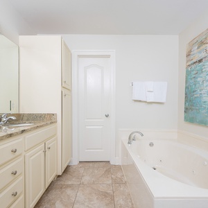 Bright and inviting master bathroom featuring a jetted tub, elegant granite countertops, and soothing coastal artwork