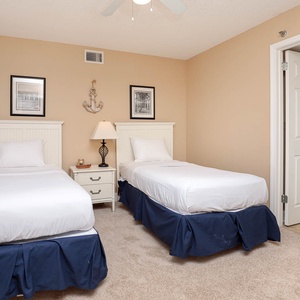 This guest bedroom features two twin beds with white linens, a bedside lamp, and beach decor on the walls