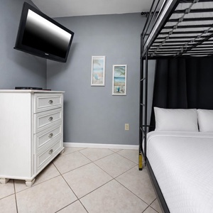 Cozy guest bedroom featuring a stylish queen bunk bed, a flat-screen TV, and beach-themed artwork for a relaxing getaway