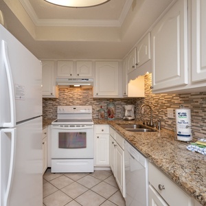 This kitchen features white cabinetry, granite countertops, and essential appliances, including a convenient coffee maker