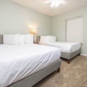 Rest comfortably in this inviting guest bedroom featuring two queen beds and a warm ambiance from the bedside lamp