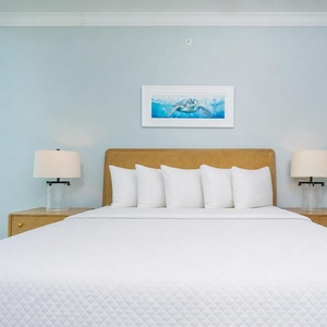 Coastal guest bedroom featuring a king bed, bedside lamps, and large windows with stunning beach views