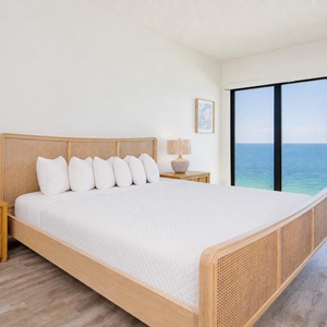 Bright and airy master bedroom featuring a king bed with plush pillows and views of the sparkling sea through large windows
