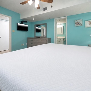 Bright turquoise walls complement the inviting king bed, while a mounted TV and dresser enhance the room's functionality