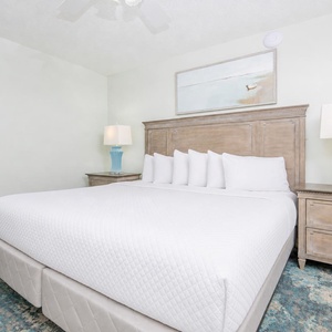 Spacious bedroom features a king bed, a decorative blue lamp, and soft area rug for added comfort