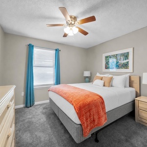 Vibrant guest room featuring a queen bed with an orange throw, complemented by turquoise curtains and a decorative lamp