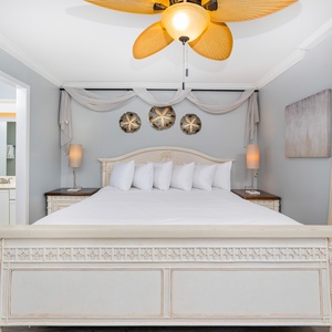 The master bedroom features a large bed with white linens, stylish lamps, and coastal decor for a relaxing retreat