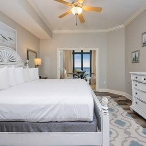 The master bedroom features a plush king bed, a wall-mounted TV, and a lovely view of the beachfront through large windows