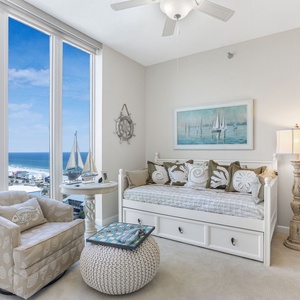 This cozy room features a daybed with a trundle, decorative pillows, a soft chair, and a beach view through large windows